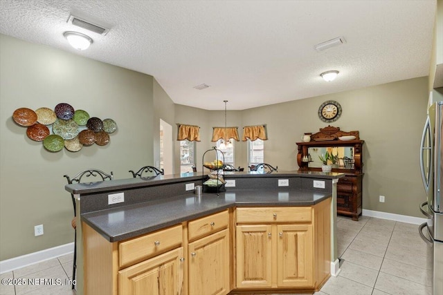 kitchen with light tile patterned floors, stainless steel fridge, hanging light fixtures, a textured ceiling, and a center island with sink