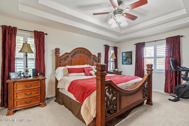 bedroom with ceiling fan, a tray ceiling, and light carpet