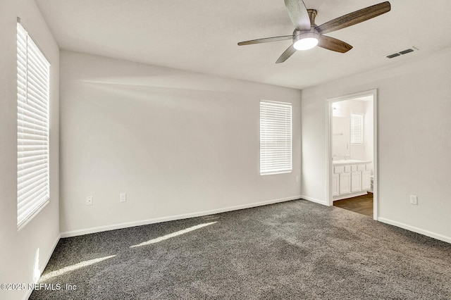 unfurnished bedroom featuring ceiling fan, ensuite bathroom, and dark colored carpet