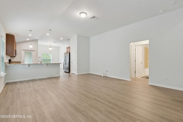 unfurnished living room featuring lofted ceiling, sink, and light hardwood / wood-style flooring