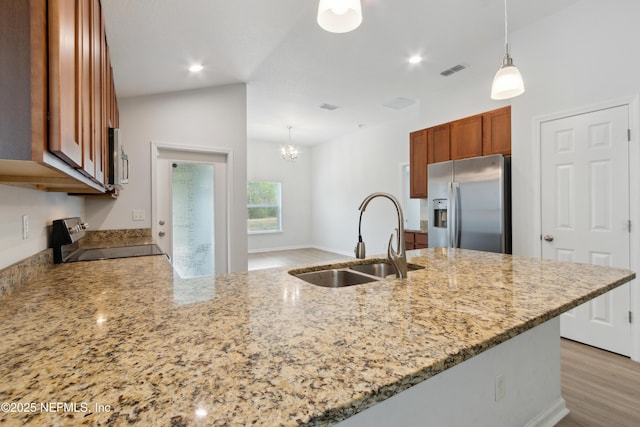 kitchen with stainless steel fridge, hanging light fixtures, light stone countertops, range, and sink