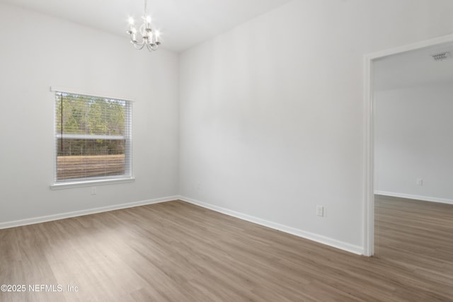 empty room featuring wood-type flooring and a chandelier