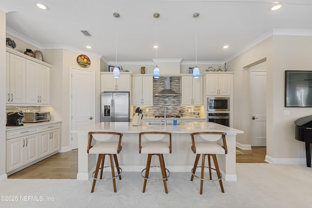 kitchen with stainless steel appliances, an island with sink, pendant lighting, and wall chimney exhaust hood