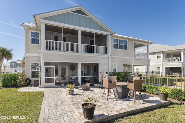 back of property with a lawn, a sunroom, a patio, and an outdoor fire pit