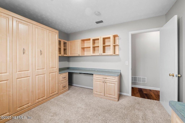 unfurnished office with a textured ceiling, light carpet, and built in desk