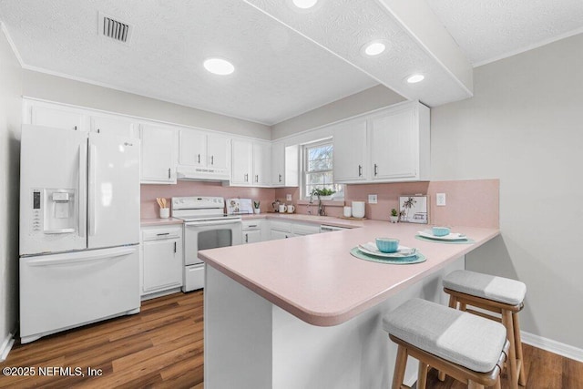 kitchen with kitchen peninsula, hardwood / wood-style flooring, white cabinets, white appliances, and a breakfast bar