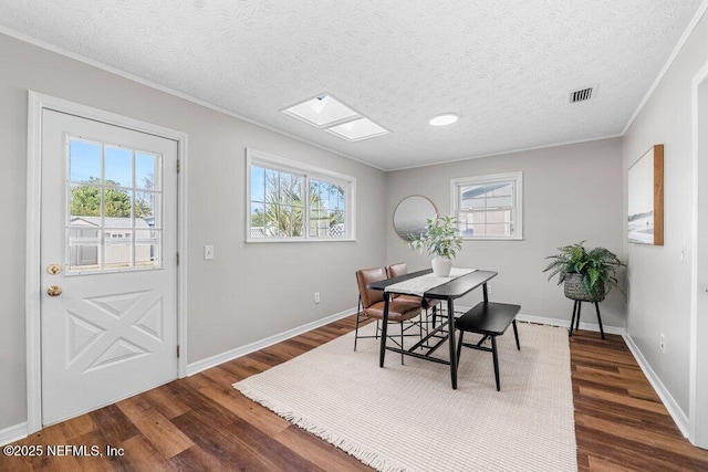 dining room featuring ornamental molding, a textured ceiling, a skylight, and dark hardwood / wood-style flooring