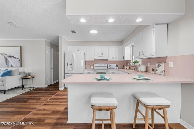 kitchen with kitchen peninsula, white appliances, a kitchen bar, and white cabinetry