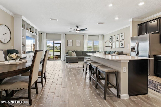 kitchen with ornamental molding, stainless steel refrigerator with ice dispenser, a breakfast bar area, and an island with sink