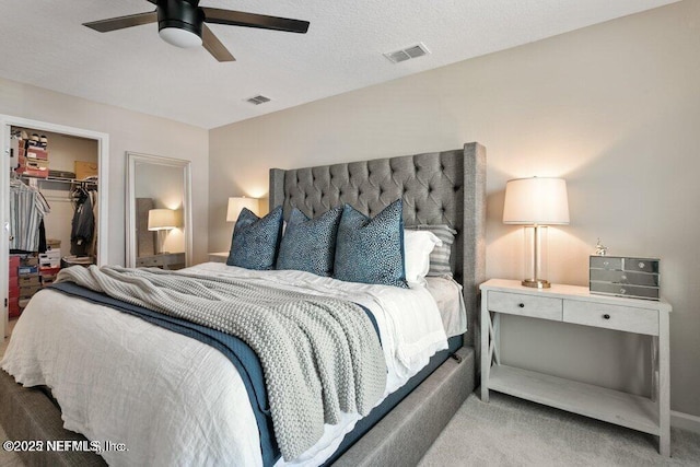 bedroom with light carpet, ceiling fan, a textured ceiling, a walk in closet, and a closet