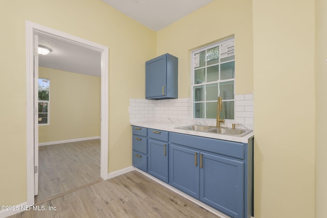 kitchen featuring a wealth of natural light, tasteful backsplash, sink, blue cabinetry, and light wood-type flooring