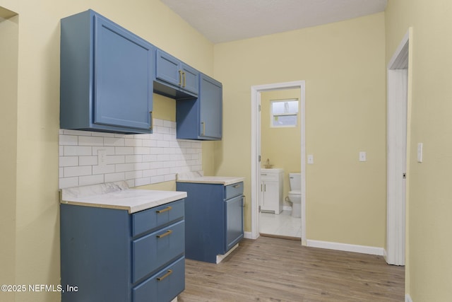 kitchen featuring blue cabinetry, backsplash, and light wood-type flooring