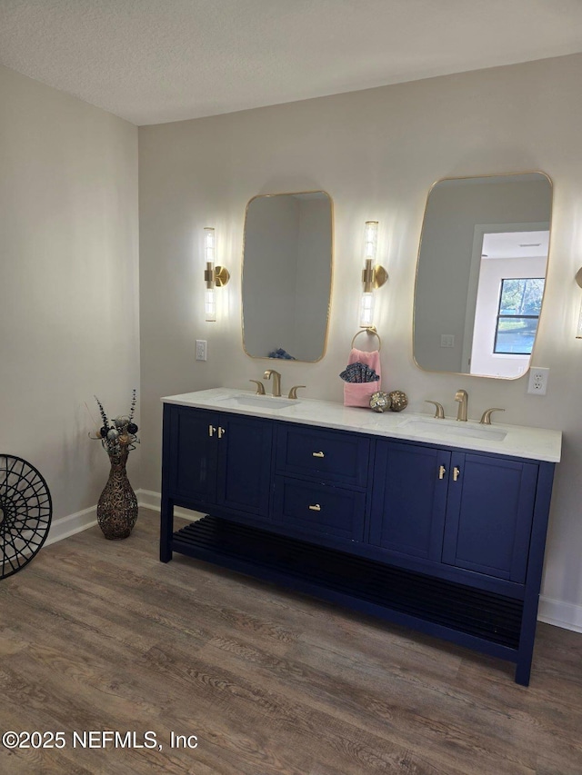 bathroom with double vanity, a sink, baseboards, and wood finished floors