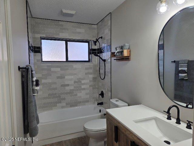 bathroom with a textured ceiling, shower / washtub combination, vanity, and toilet