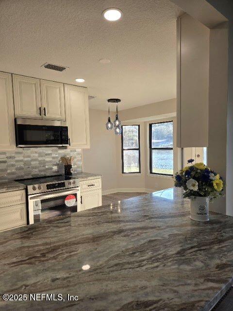 kitchen featuring tasteful backsplash, visible vents, appliances with stainless steel finishes, white cabinetry, and dark stone countertops