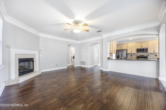 unfurnished living room with a fireplace, washer / dryer, ceiling fan, crown molding, and dark wood-type flooring