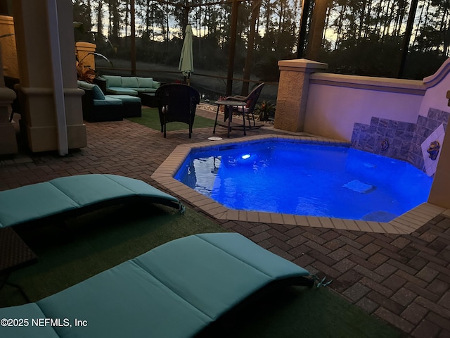 pool at dusk with a patio area, glass enclosure, and outdoor lounge area