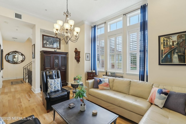 living room with baseboards, visible vents, light wood-style flooring, crown molding, and a chandelier