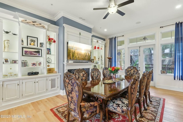 dining room featuring crown molding, a premium fireplace, light wood-style floors, ceiling fan, and baseboards