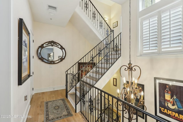 stairs with baseboards, visible vents, wood finished floors, an inviting chandelier, and a high ceiling