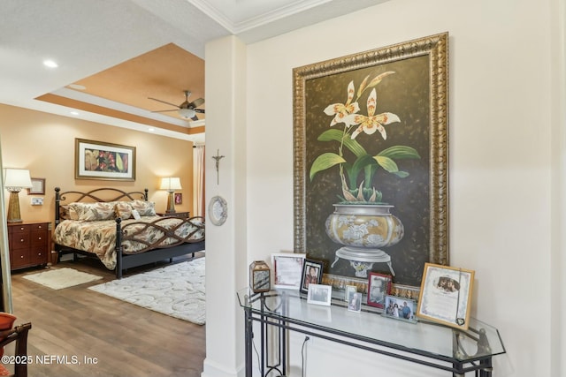 bedroom featuring a raised ceiling, ornamental molding, wood finished floors, and recessed lighting