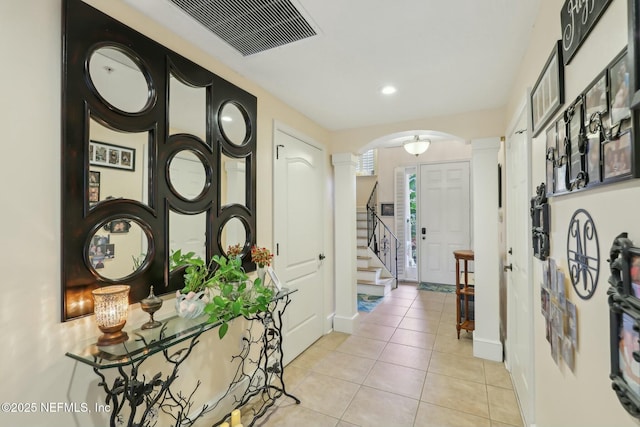 hall featuring arched walkways, light tile patterned flooring, decorative columns, and visible vents