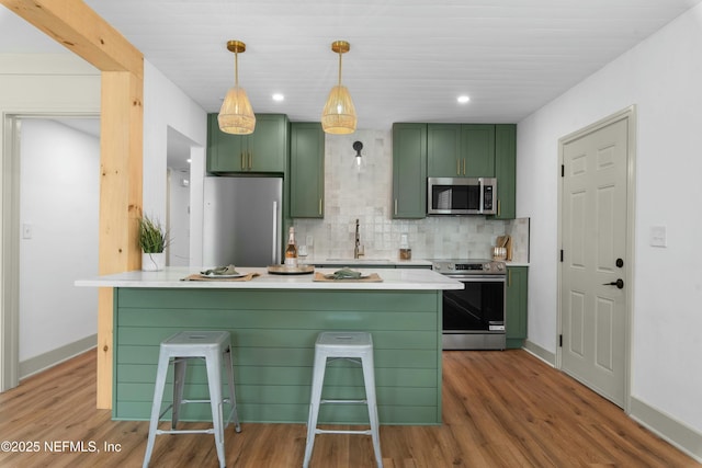 kitchen with appliances with stainless steel finishes, backsplash, hanging light fixtures, green cabinetry, and a breakfast bar