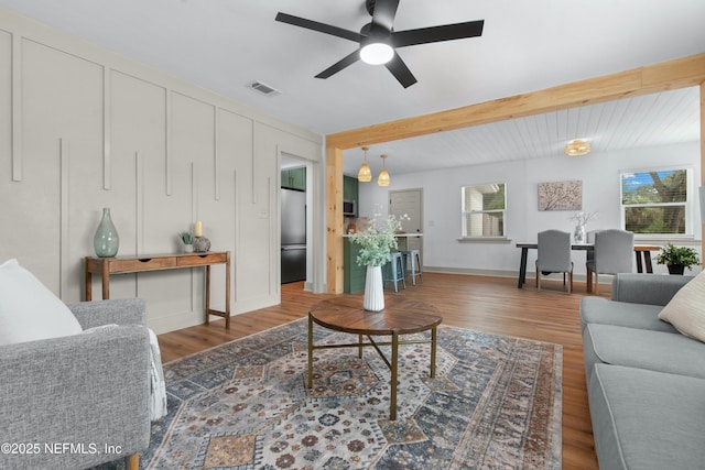 living room with ceiling fan, beam ceiling, and dark wood-type flooring