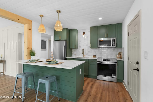 kitchen with green cabinets, hanging light fixtures, sink, a breakfast bar area, and stainless steel appliances