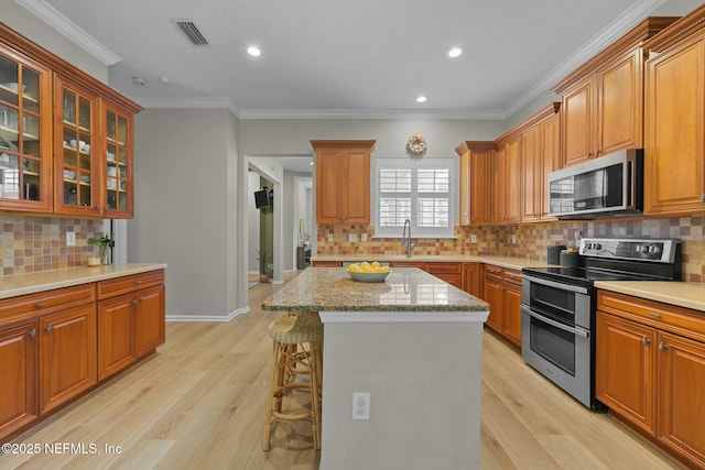 kitchen with ornamental molding, appliances with stainless steel finishes, a kitchen breakfast bar, a kitchen island, and light hardwood / wood-style floors