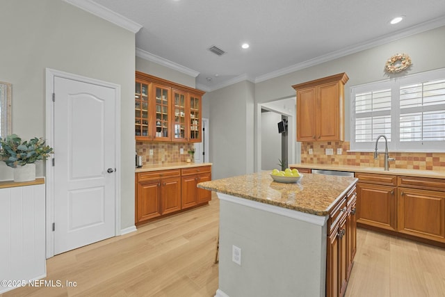 kitchen featuring a kitchen island, sink, light stone counters, crown molding, and light wood-type flooring