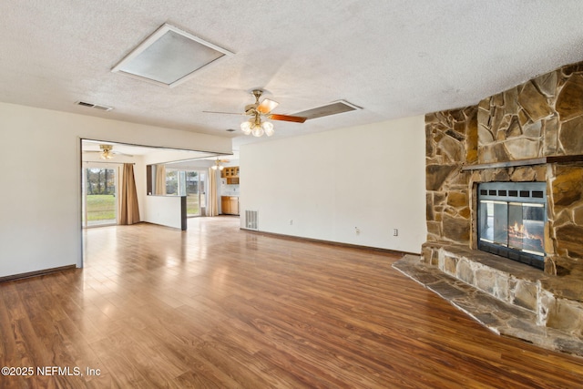 unfurnished living room with hardwood / wood-style floors, a stone fireplace, a textured ceiling, and ceiling fan