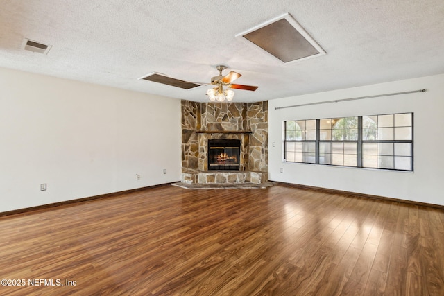 unfurnished living room with ceiling fan, a stone fireplace, hardwood / wood-style floors, and a textured ceiling