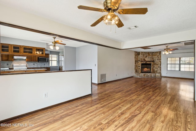 unfurnished living room with ceiling fan, a fireplace, hardwood / wood-style floors, and a textured ceiling