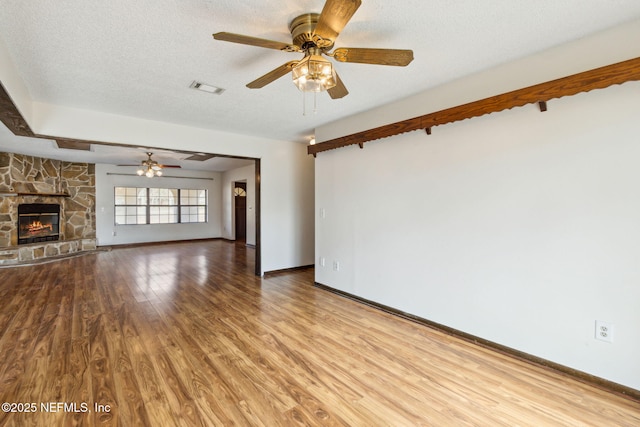 unfurnished living room featuring ceiling fan, a stone fireplace, a textured ceiling, and light wood-type flooring