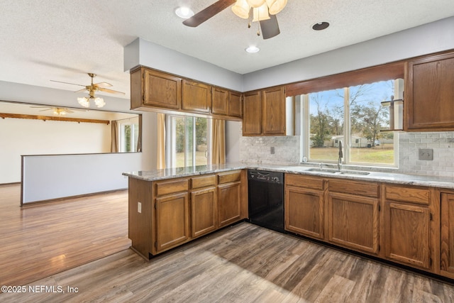 kitchen featuring sink, black dishwasher, kitchen peninsula, light stone countertops, and light hardwood / wood-style floors