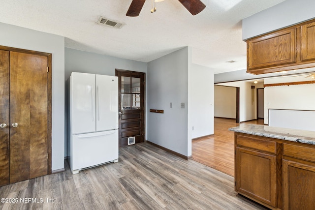 kitchen featuring light stone counters, light wood-type flooring, ceiling fan, and white refrigerator