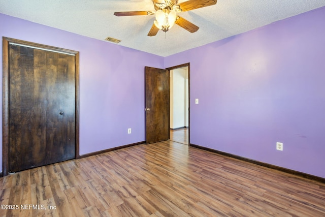 unfurnished bedroom featuring ceiling fan, a closet, light hardwood / wood-style flooring, and a textured ceiling