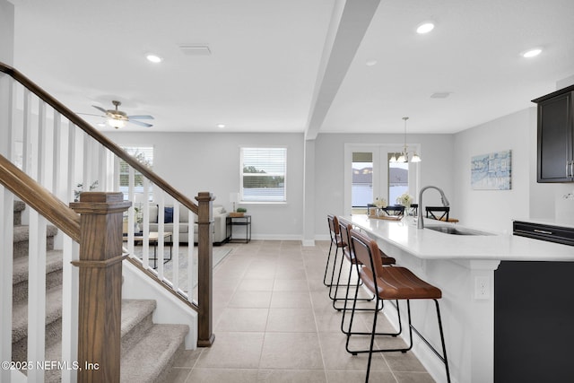 kitchen with ceiling fan with notable chandelier, pendant lighting, sink, light tile patterned floors, and a center island with sink