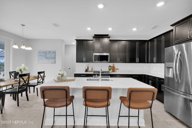 kitchen featuring sink, hanging light fixtures, light tile patterned floors, stainless steel appliances, and a kitchen island with sink