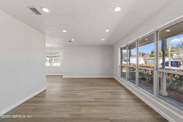 spare room featuring a healthy amount of sunlight, hardwood / wood-style flooring, and a textured ceiling