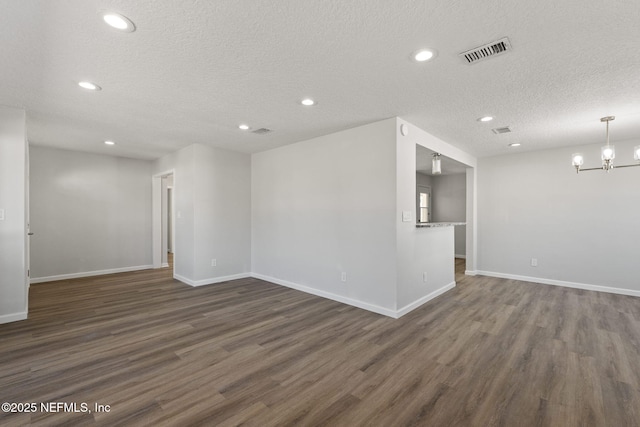 spare room featuring dark wood-type flooring, a chandelier, and a textured ceiling