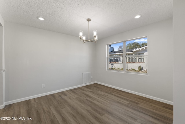 empty room featuring dark wood-type flooring, a chandelier, and a textured ceiling