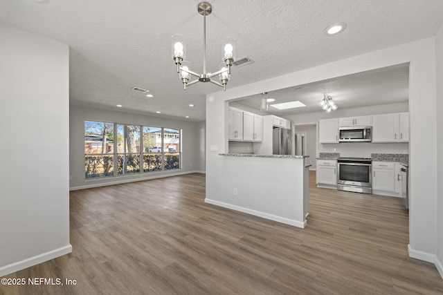 kitchen with white cabinetry, appliances with stainless steel finishes, dark hardwood / wood-style floors, kitchen peninsula, and light stone countertops