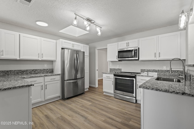 kitchen with sink, white cabinetry, stainless steel appliances, a textured ceiling, and dark stone counters