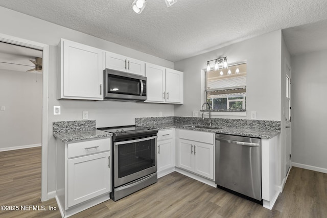 kitchen with sink, a textured ceiling, appliances with stainless steel finishes, light stone countertops, and white cabinets