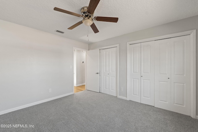 unfurnished bedroom with light carpet, two closets, a textured ceiling, and ceiling fan