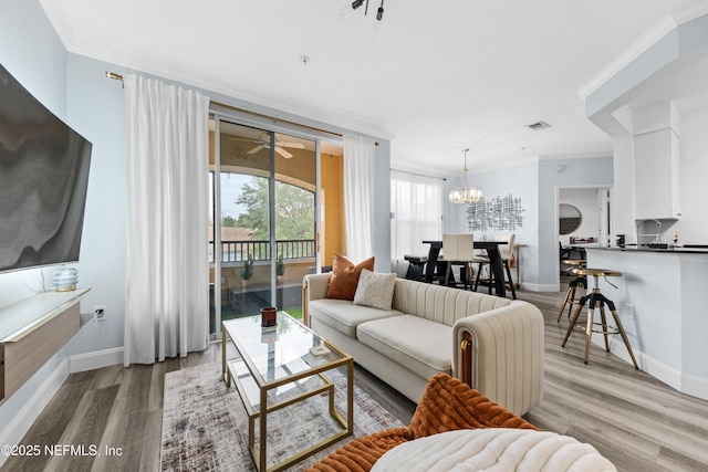 living room with ceiling fan with notable chandelier, light hardwood / wood-style flooring, and ornamental molding