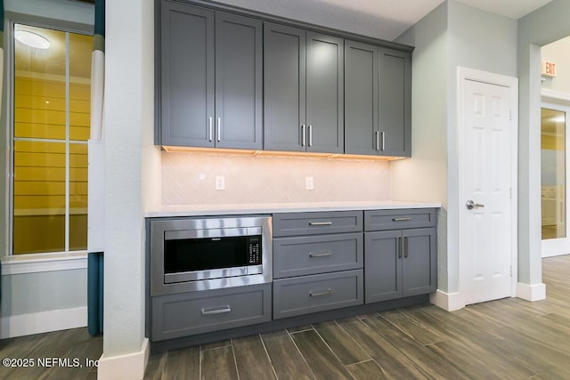 bar featuring stainless steel microwave, gray cabinetry, dark hardwood / wood-style flooring, and tasteful backsplash