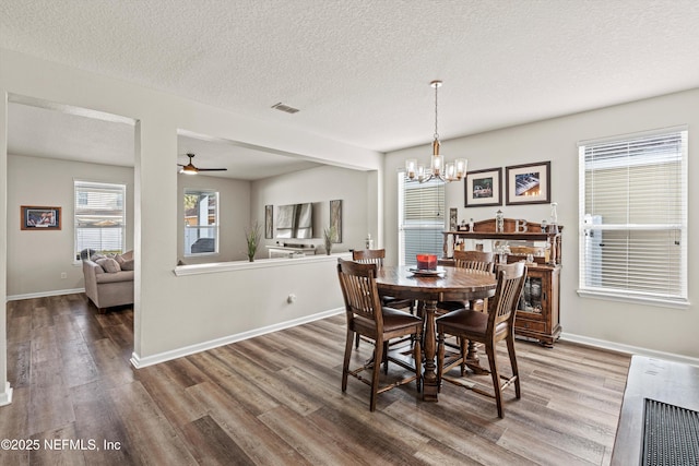 dining space featuring wood-type flooring, ceiling fan with notable chandelier, and a textured ceiling